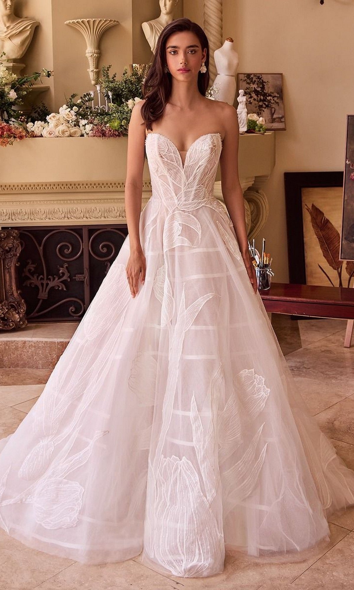 A woman stands indoors wearing the Andrea and Leo WL043 long wedding dress, a strapless gown with a sweetheart neckline, fitted bodice, and floral-patterned tulle A-line skirt.